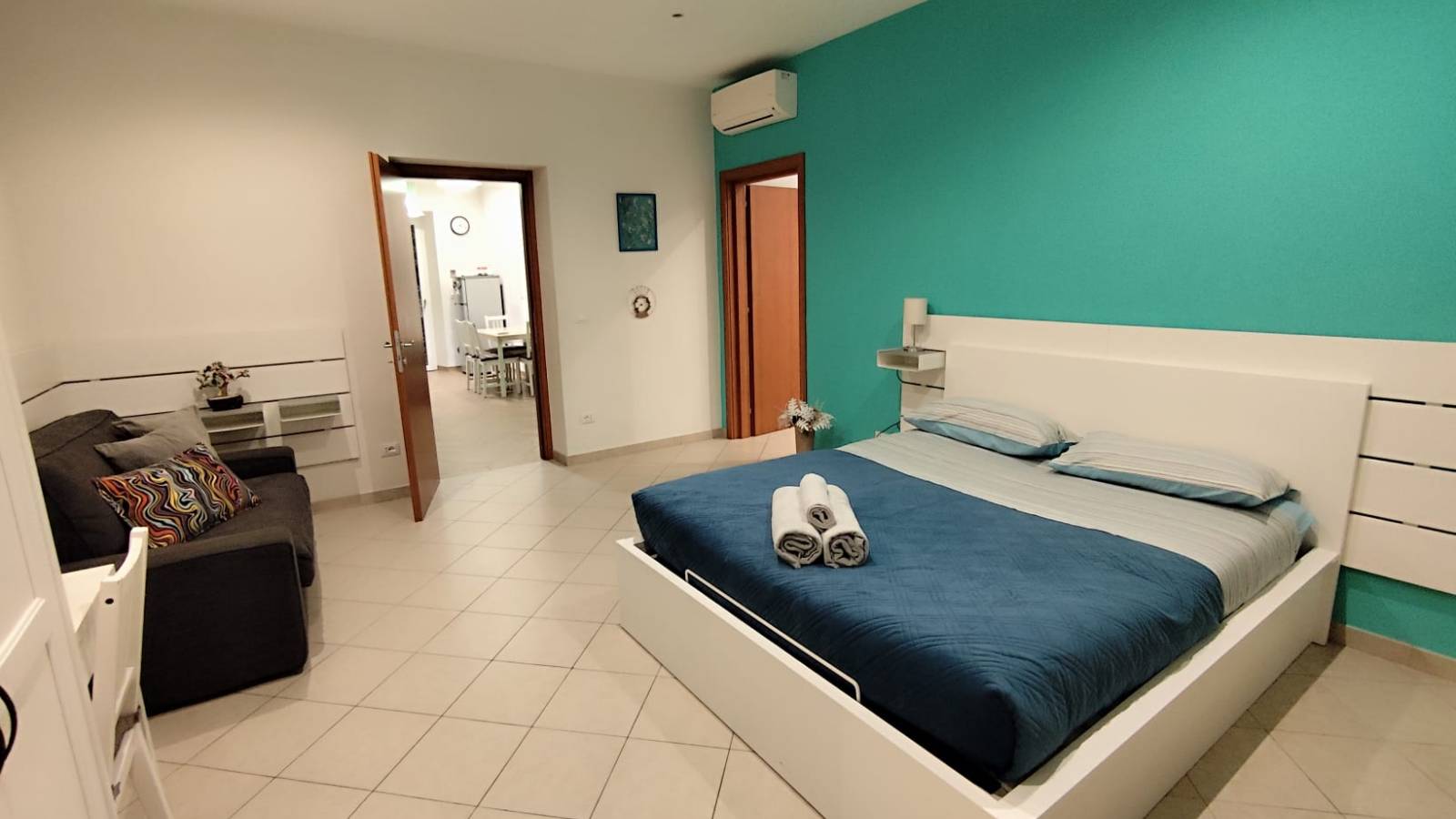 Alt Text: Spacious and bright master bedroom with a queen-size bed, vibrant "full of colour" decor, and air conditioning at Roma Tourist Home, Rome.